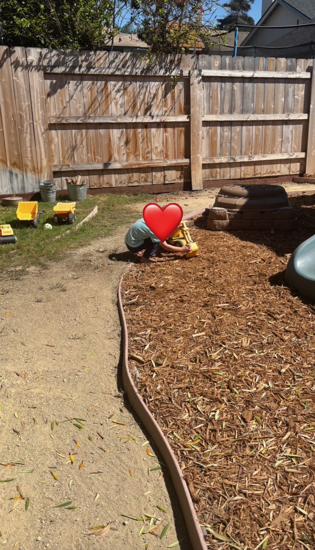 A preschooler playing with trucks in the wood-chip play yard at Heidi's House Childcare