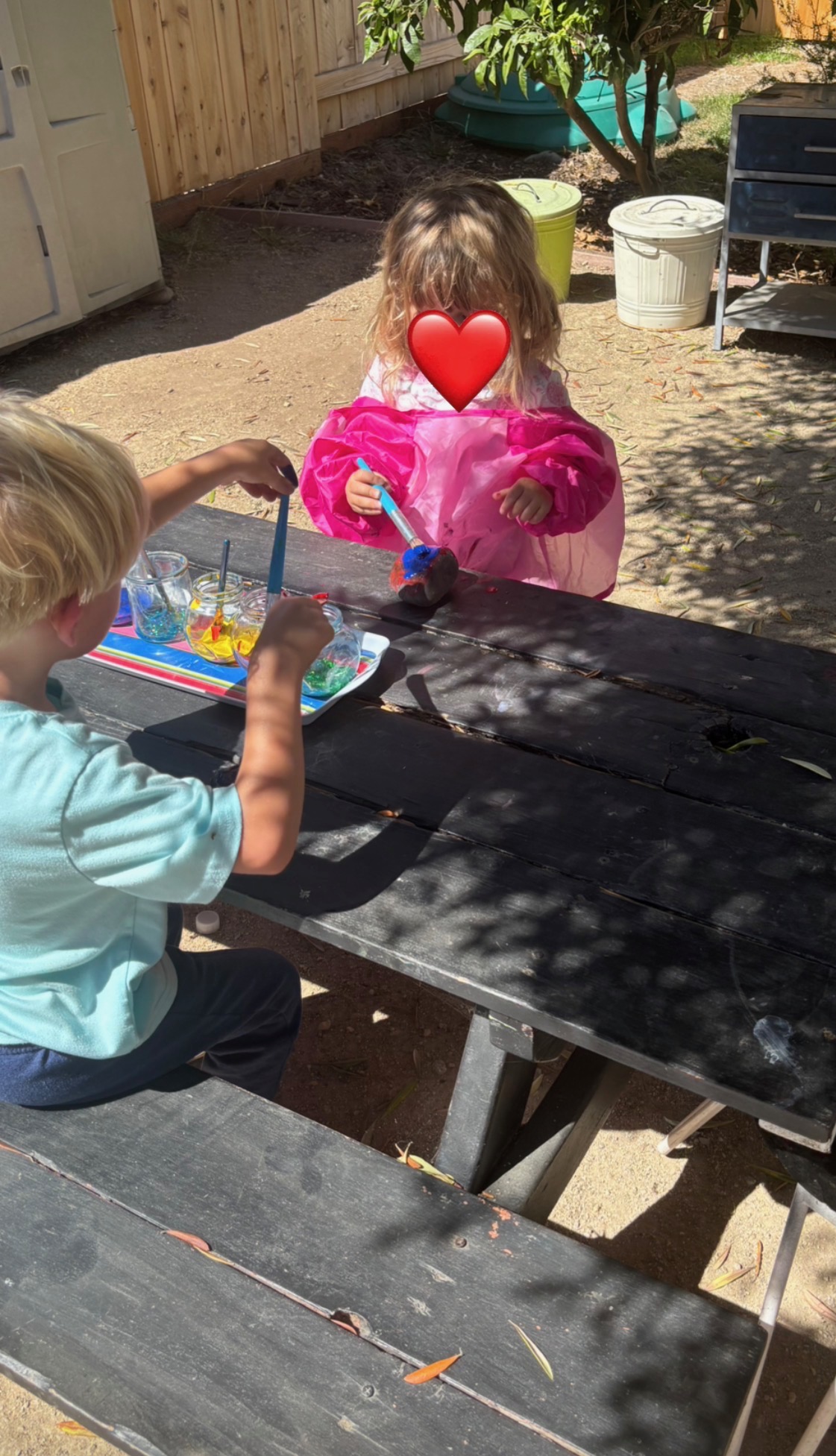 Children painting with watercolors at a shaded outdoor table at Heidi's House Childcare